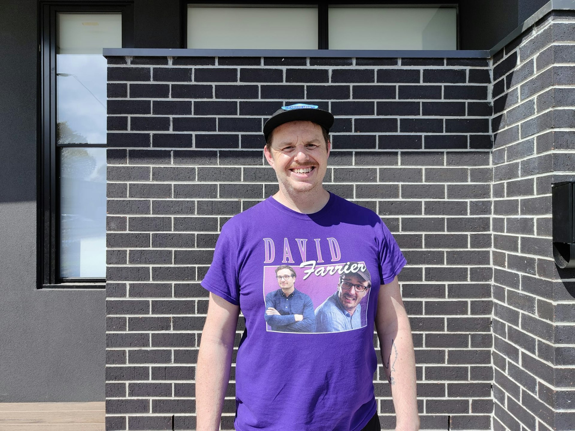 Dave stands smiling in front of a brick wall.
